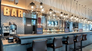 A bar area with a brick wall, bar stools, and hanging light fixtures. - Premier Inn Berlin Alexanderplatz (Berlin)