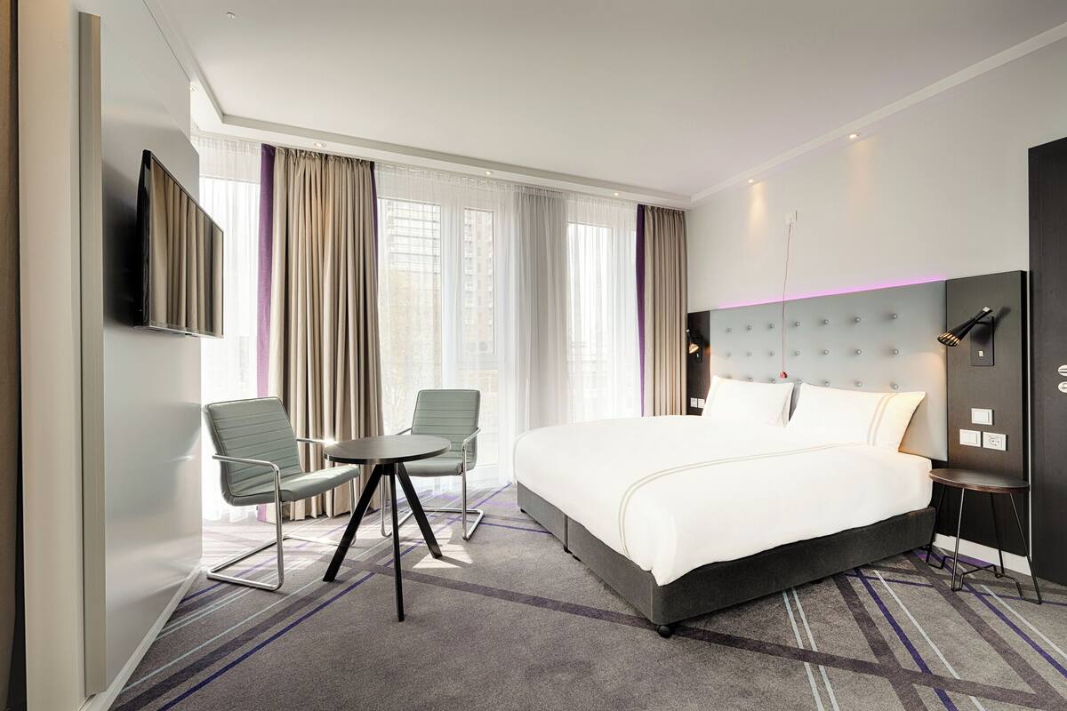 Una habitación de hotel moderna con una cama grande, un escritorio, dos sillas y un televisor.