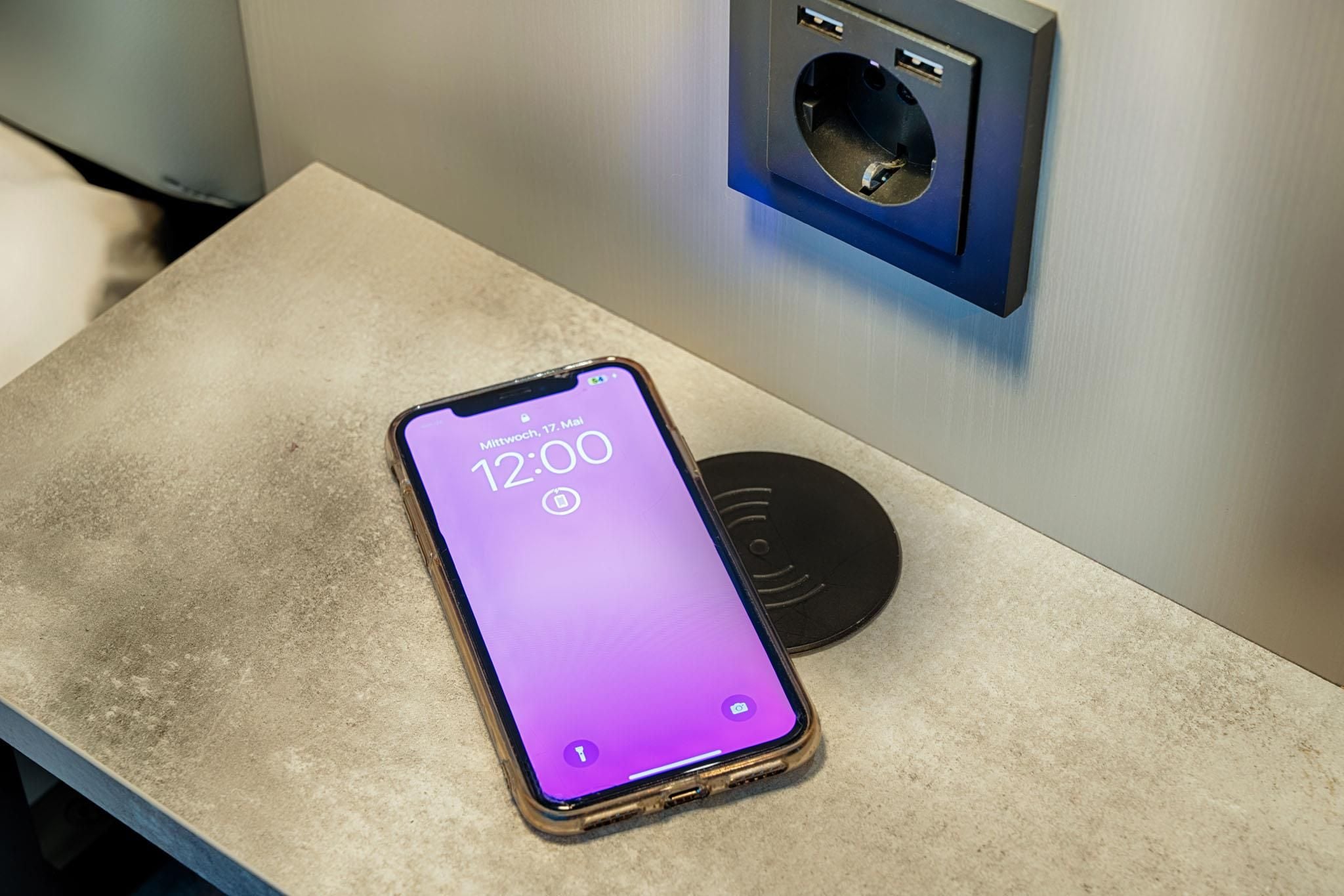 A smartphone on a table with a charging cable and a wall socket.