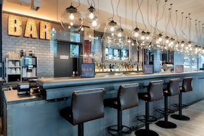 A bar area with a brick wall, bar stools, and hanging light fixtures. - Premier Inn Berlin Alexanderplatz (Berlin)