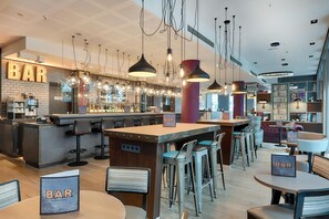 A bar area with multiple seating options, including bar stools and round tables, and a bar counter with a sign. - Premier Inn Berlin Alexanderplatz (Berlin)