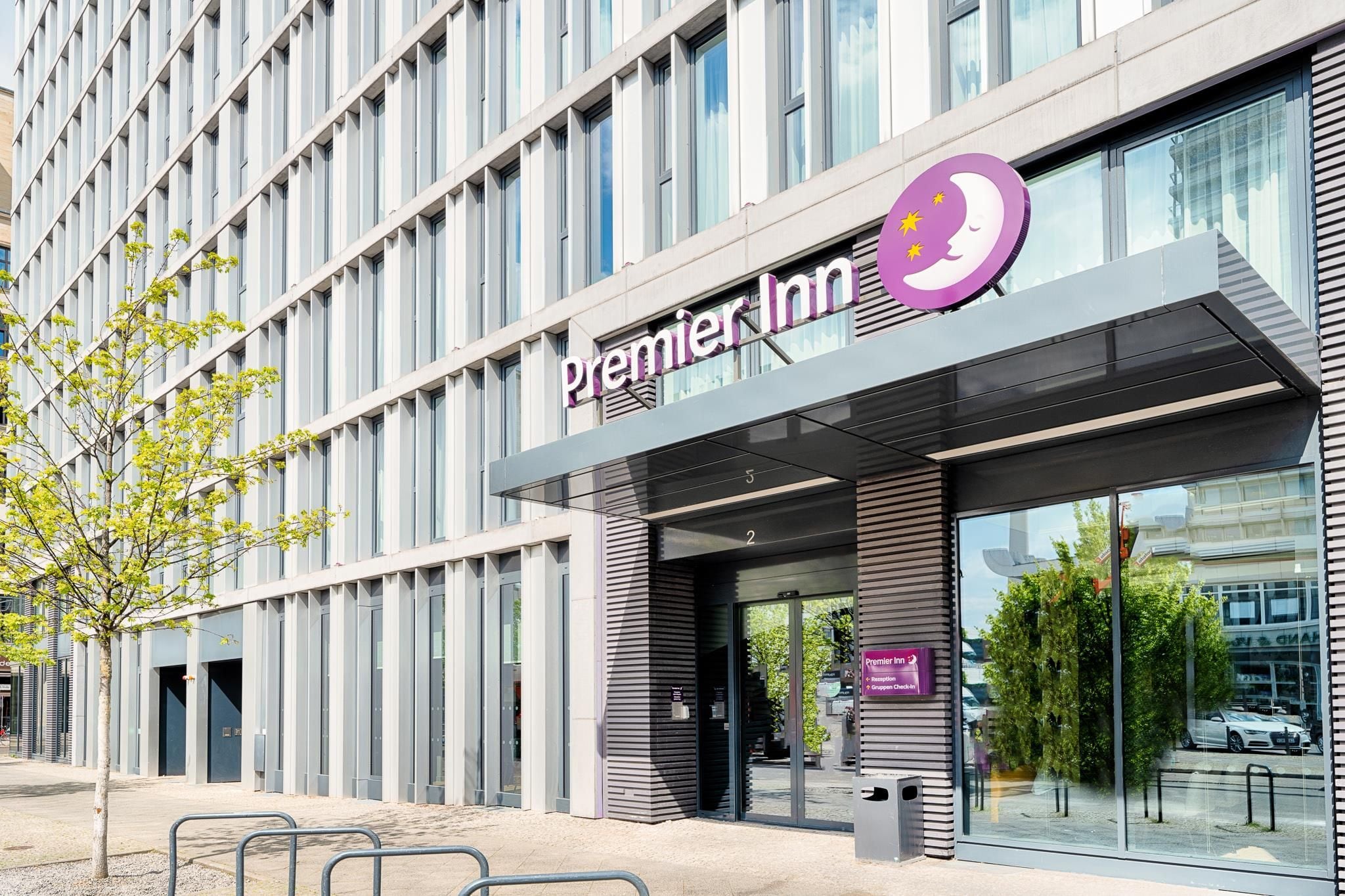 Un edificio moderno con un llamativo letrero de Premier Inn, ventanas amplias y un árbol en primer plano.