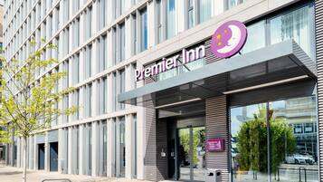 Un edificio moderno con un llamativo letrero de Premier Inn, ventanas amplias y un árbol en primer plano.