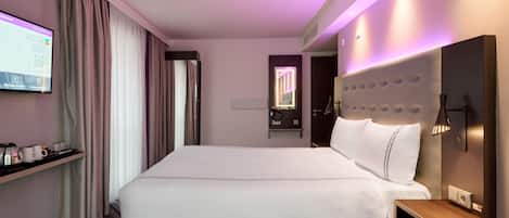 Una habitación de hotel con una cama grande, un televisor montado en la pared, una mesita de noche y un buró.