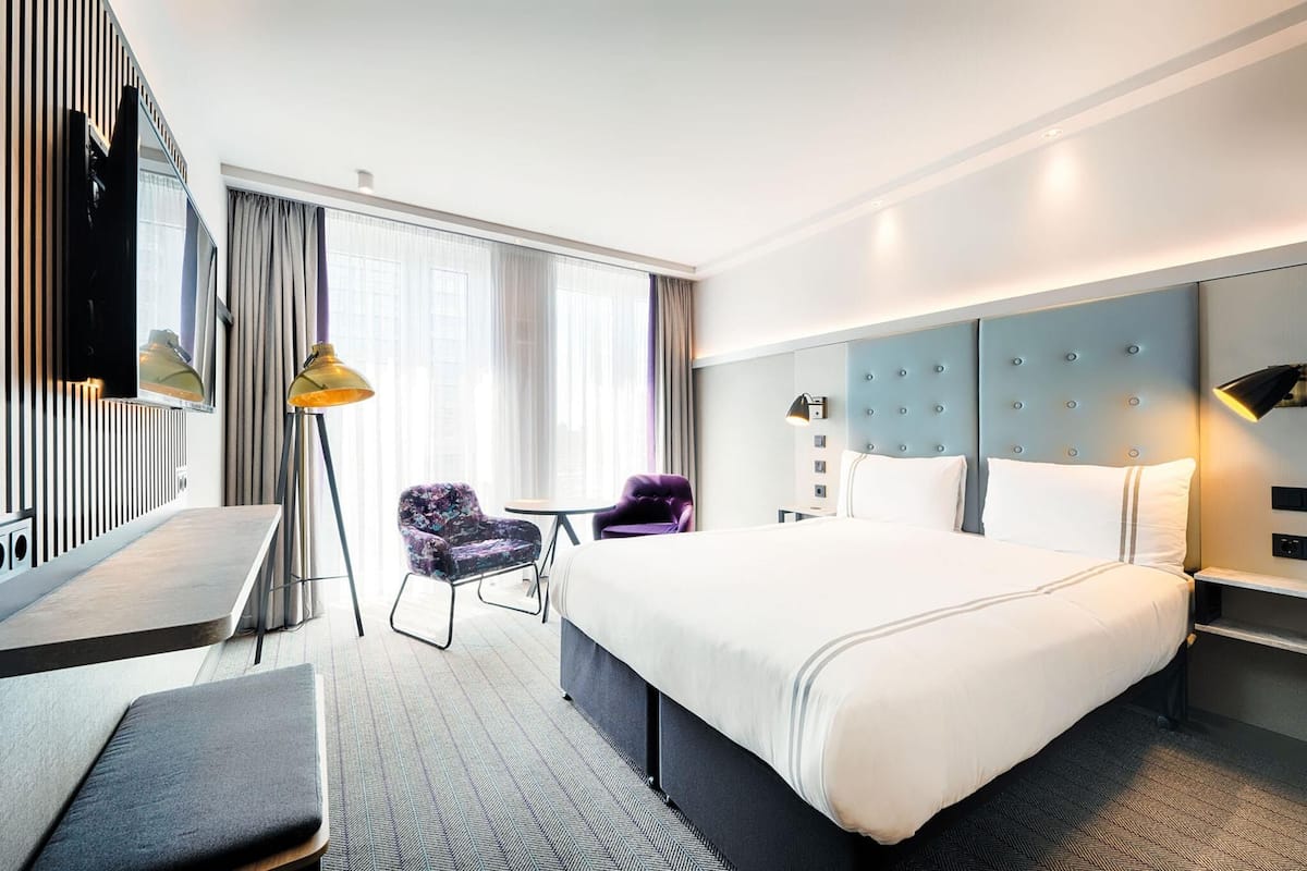 Una habitación de hotel con una cama grande, un escritorio, una silla, un televisor y una ventana con cortinas.