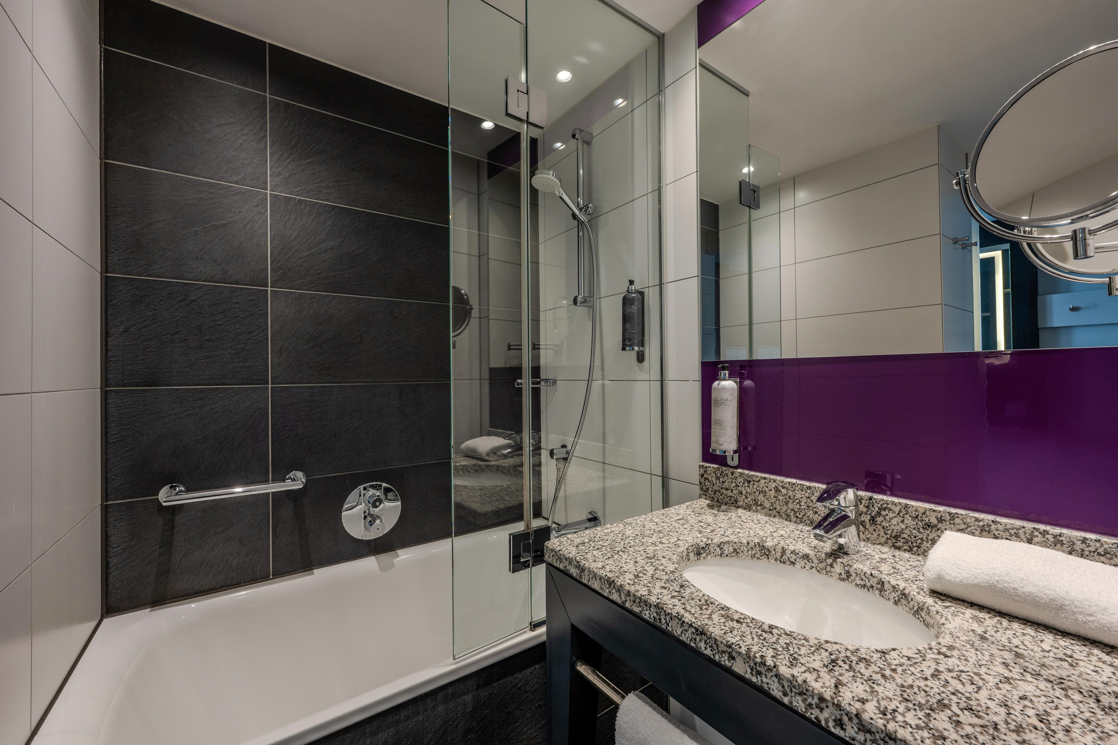 A modern bathroom with a glass-enclosed shower, a white bathtub, and a granite countertop sink.