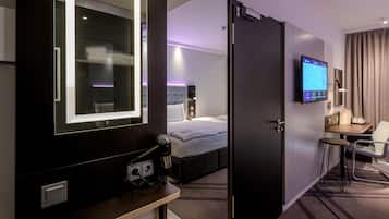 A hotel room with a bed, a desk with a chair, a TV, and a mirror.