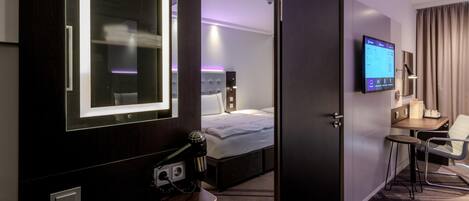 Una habitación de hotel con cama, escritorio con silla, televisión y espejo.