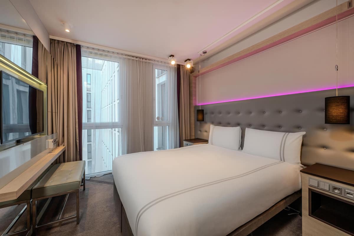 Una habitación de hotel con una cama grande, un escritorio, un televisor y una ventana con cortinas.