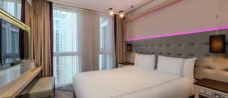 Una habitación de hotel con una cama grande, un escritorio, un televisor y una ventana con cortinas.