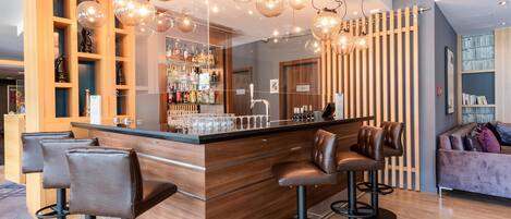A modern bar area with wooden bar stools, a counter with bar tools, and a wine rack.
