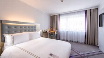 A hotel room with a large bed, a desk, a chair, and a TV.