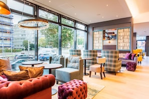 A modern interior with large windows, comfortable seating, and a visible bookshelf. - Premier Inn Stuttgart Feuerbach (Stuttgart)