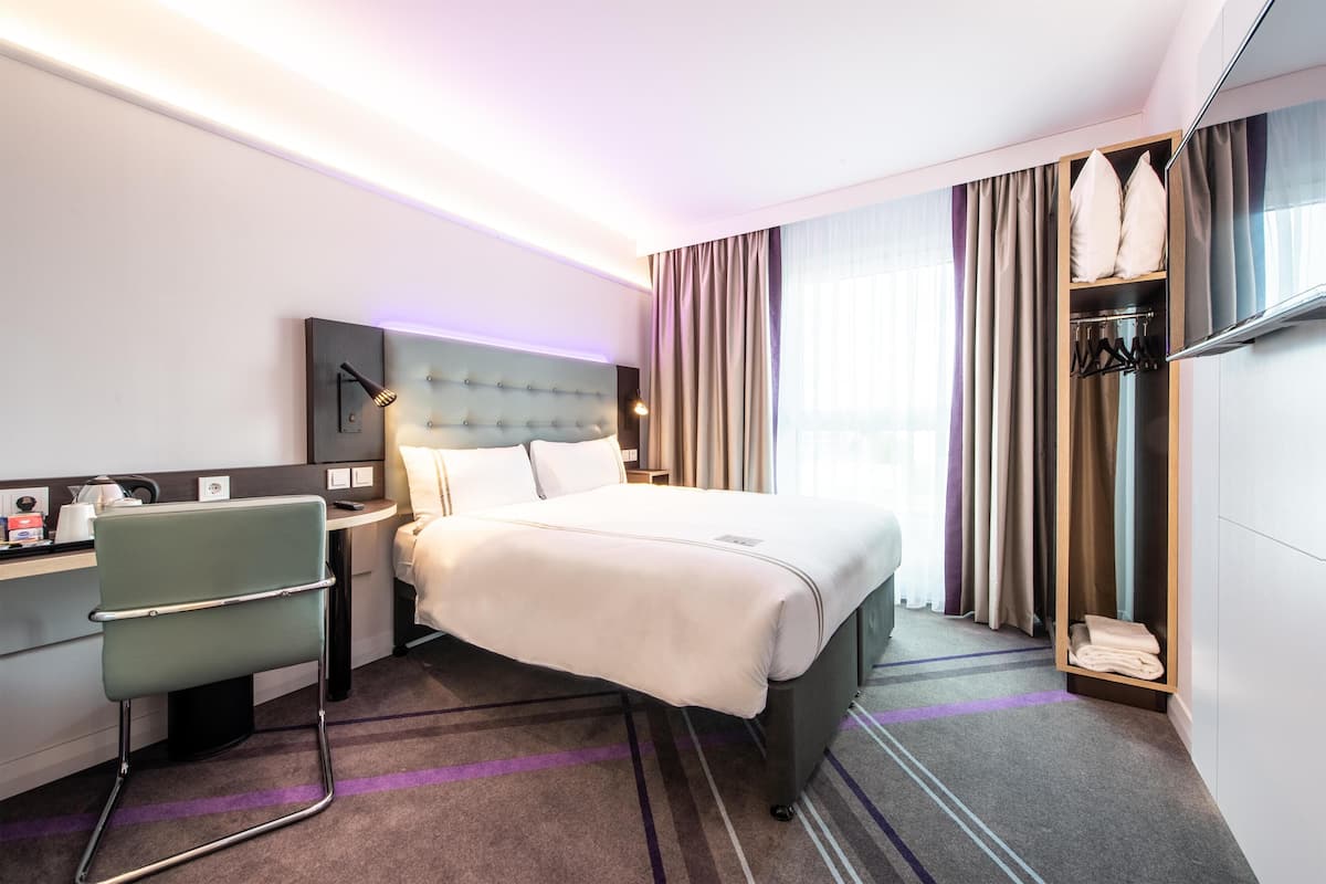 Una habitación de hotel con cama, escritorio, silla, armario y televisor.