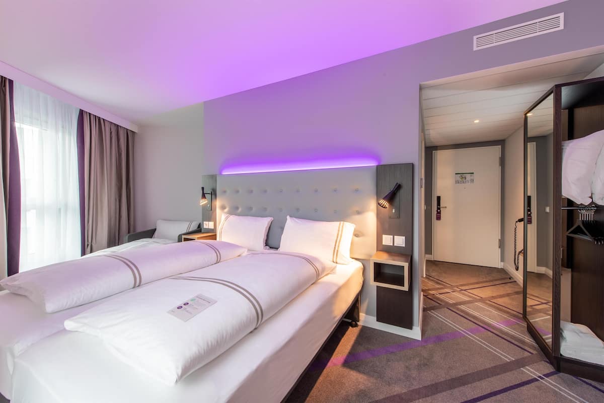 Una habitación de hotel con una cama grande, mesitas de noche, un armario y un baño visible a través de una puerta abierta.