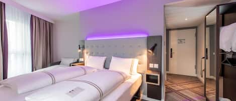 Una habitación de hotel con una cama grande, mesitas de noche, un armario y un baño visible a través de una puerta abierta.
