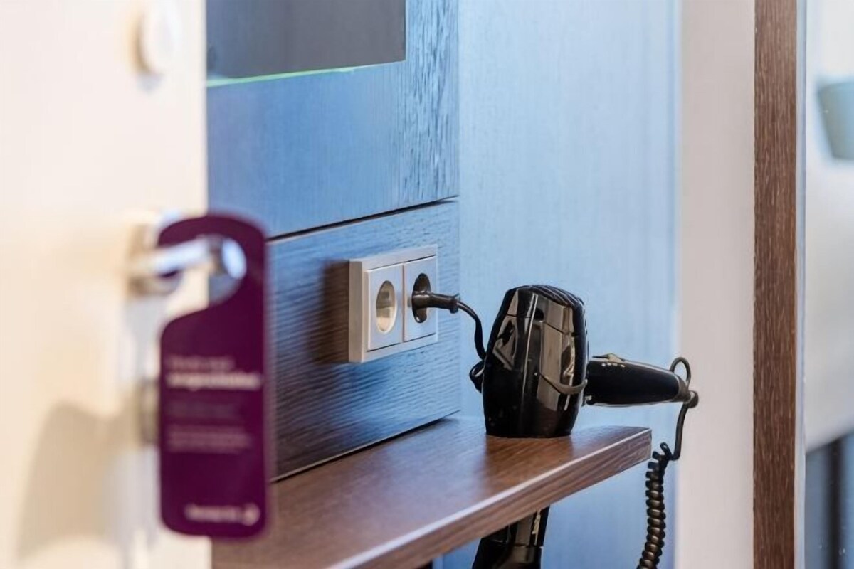 A hotel room with a telephone on a wooden shelf, a purple keycard holder, and a wall-mounted light switch.