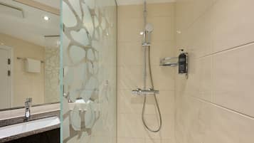 A modern bathroom with a glass shower enclosure, a handheld showerhead, a wall-mounted faucet, and a soap dispenser.