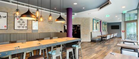 Un restaurante moderno con mesas comunitarias largas, taburetes de bar, iluminación colgante y una pared de ladrillo.