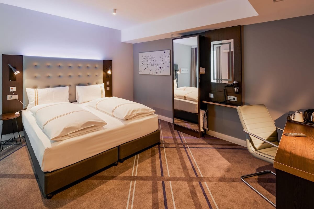 Una habitación de hotel con una cama grande, una mesita de noche, una silla, un escritorio y un espejo.