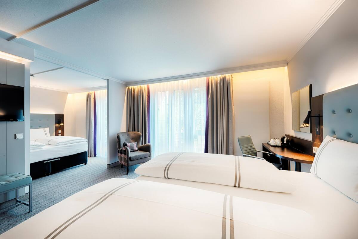 Habitación de hotel con una cama grande, un escritorio, una silla, un televisor y una ventana con cortinas.