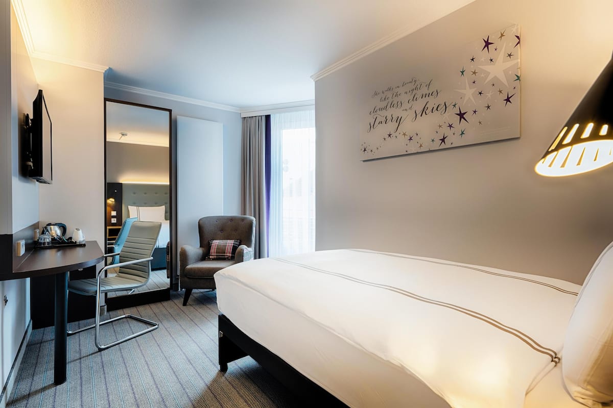 Habitación de hotel con cama, escritorio, silla y una pared con una cita alusiva a una noche estrellada.