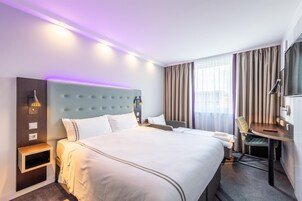 Ein Hotelzimmer mit einem großen Bett, Nachttischen, einem Schreibtisch und einem Sessel.