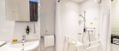 A modern bathroom with a sink, mirror, shower, and grab bars.