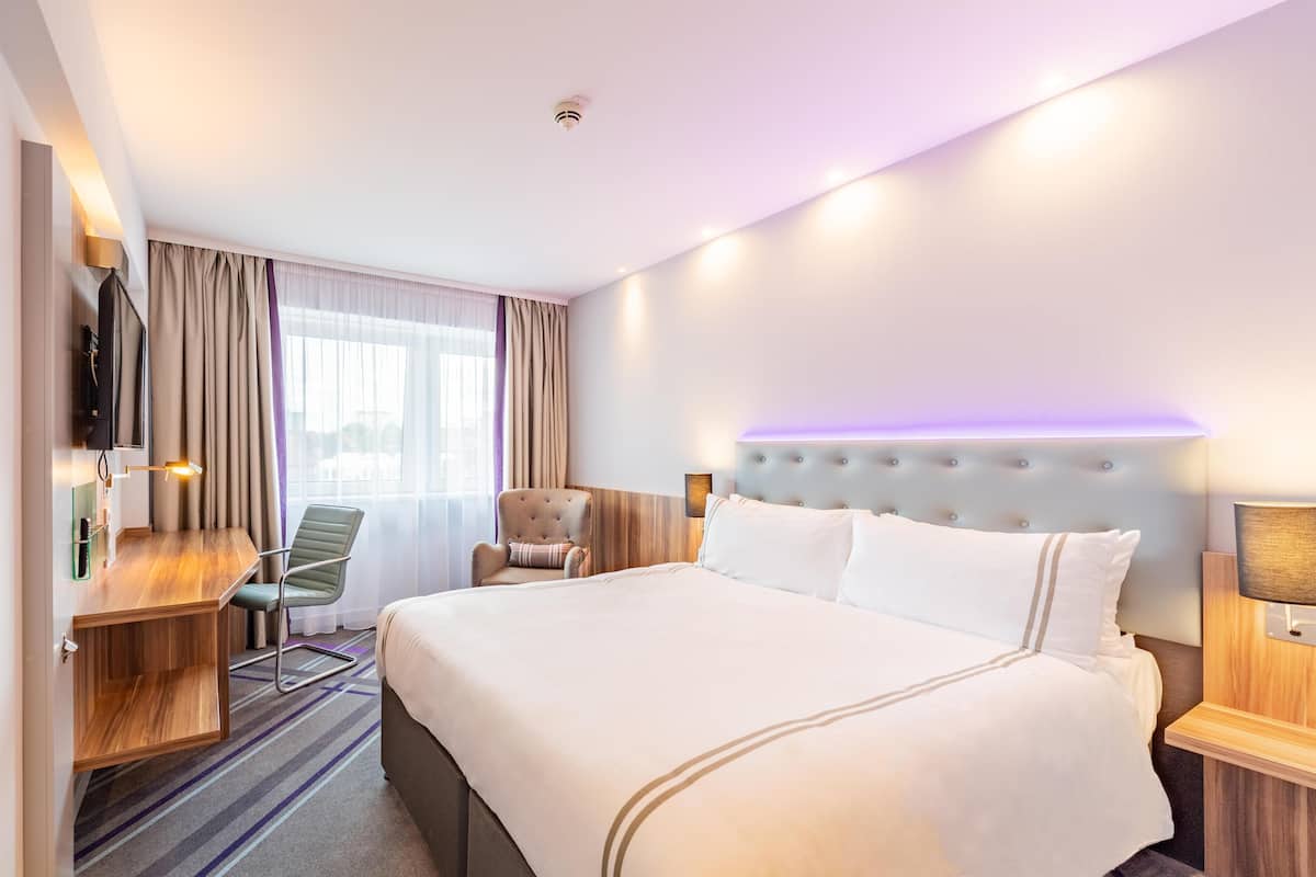 A hotel room with a bed, a desk, a chair, a TV, and a window with curtains.