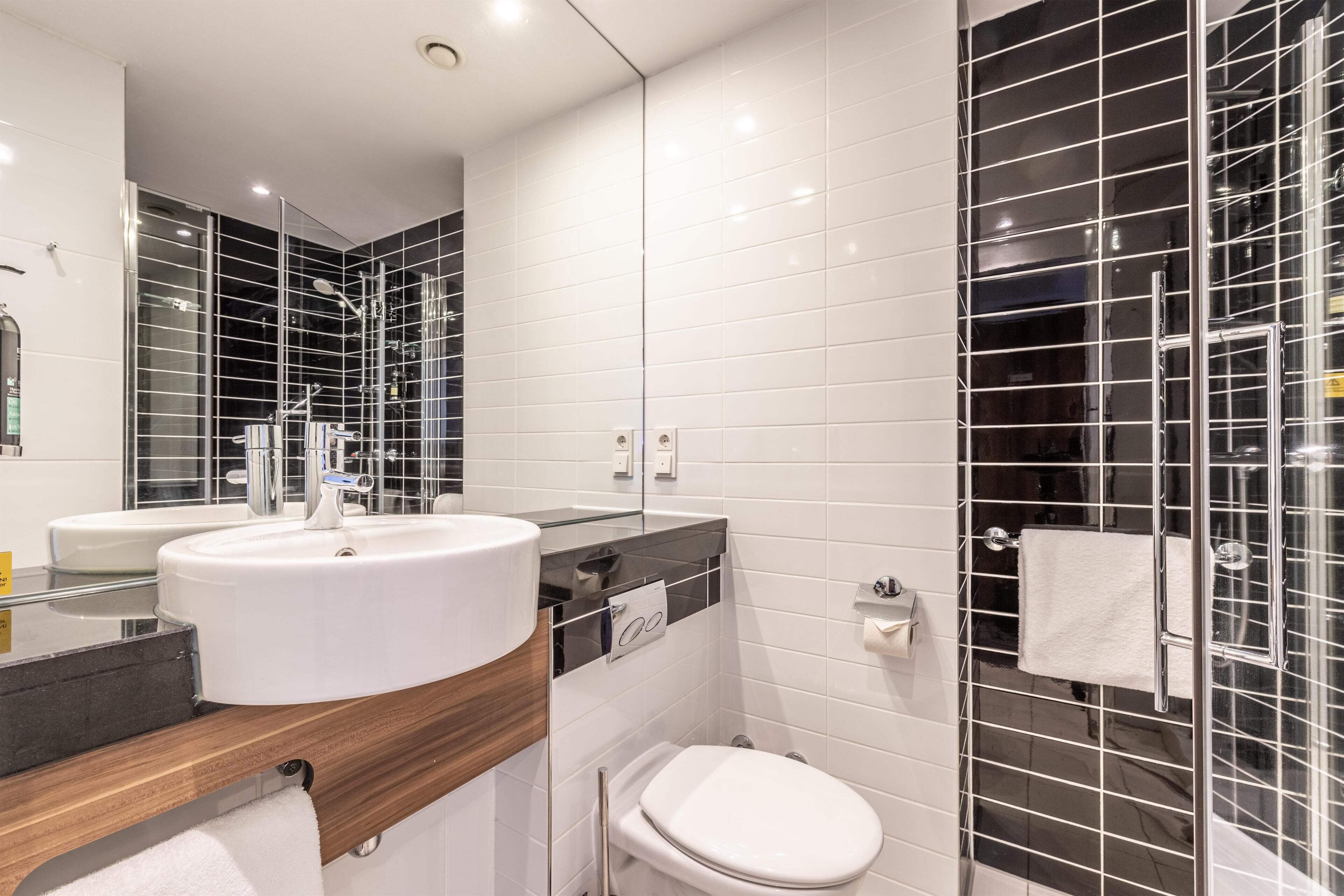 Ein modernes Badezimmer mit einem großen, weißen Waschbecken, einem Spiegel und einer Duschkabine aus Glas.
