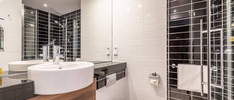 Un baño moderno con un lavamanos grande blanco, un espejo y una cabina de ducha de vidrio.