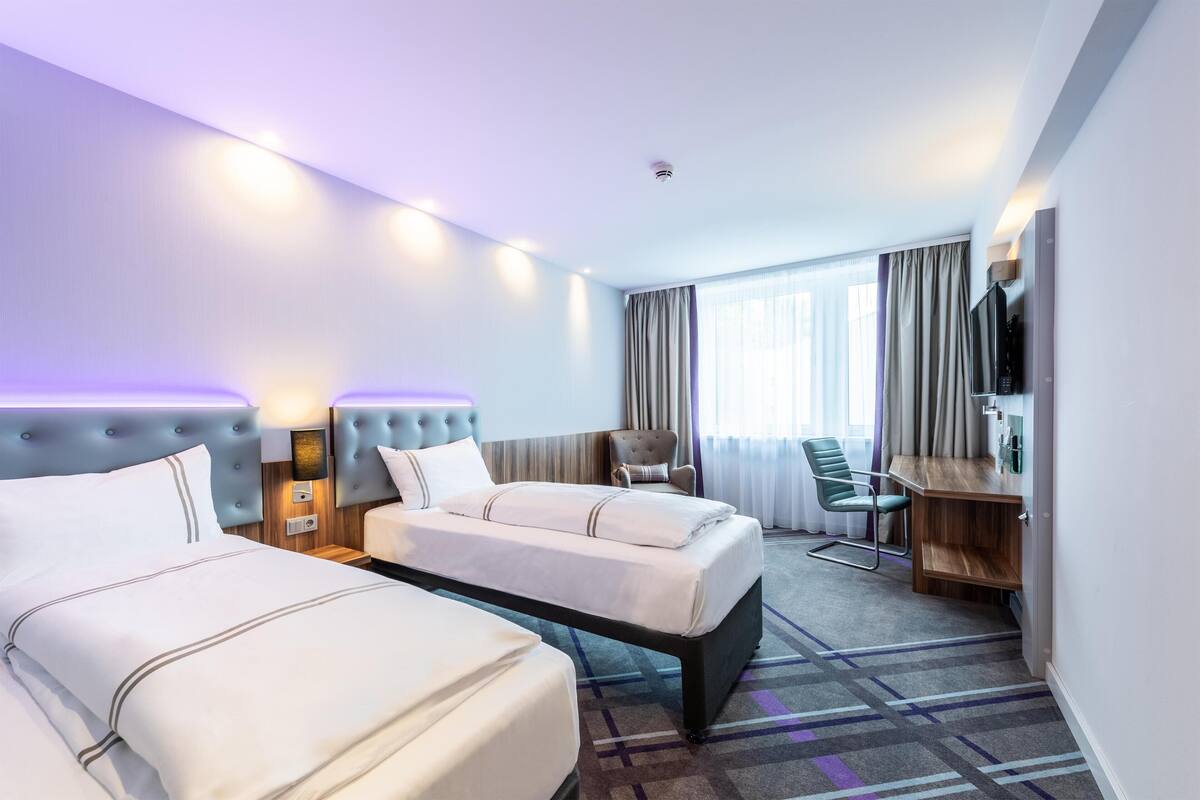 A hotel room with two beds, a desk, a chair, a television, and a window with curtains.