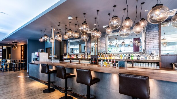 Una zona de bar con taburetes, una barra y lámparas esféricas colgantes.