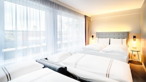 A hotel room with two beds, a large window with sheer curtains, a headboard with a light fixture, and a small bedside table with a lamp. - Premier Inn Berlin City Süd (Berlin)