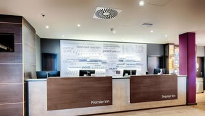 A hotel reception desk with two counters, a large wall clock, and a ceiling light fixture. - Premier Inn Berlin City Süd (Berlin)