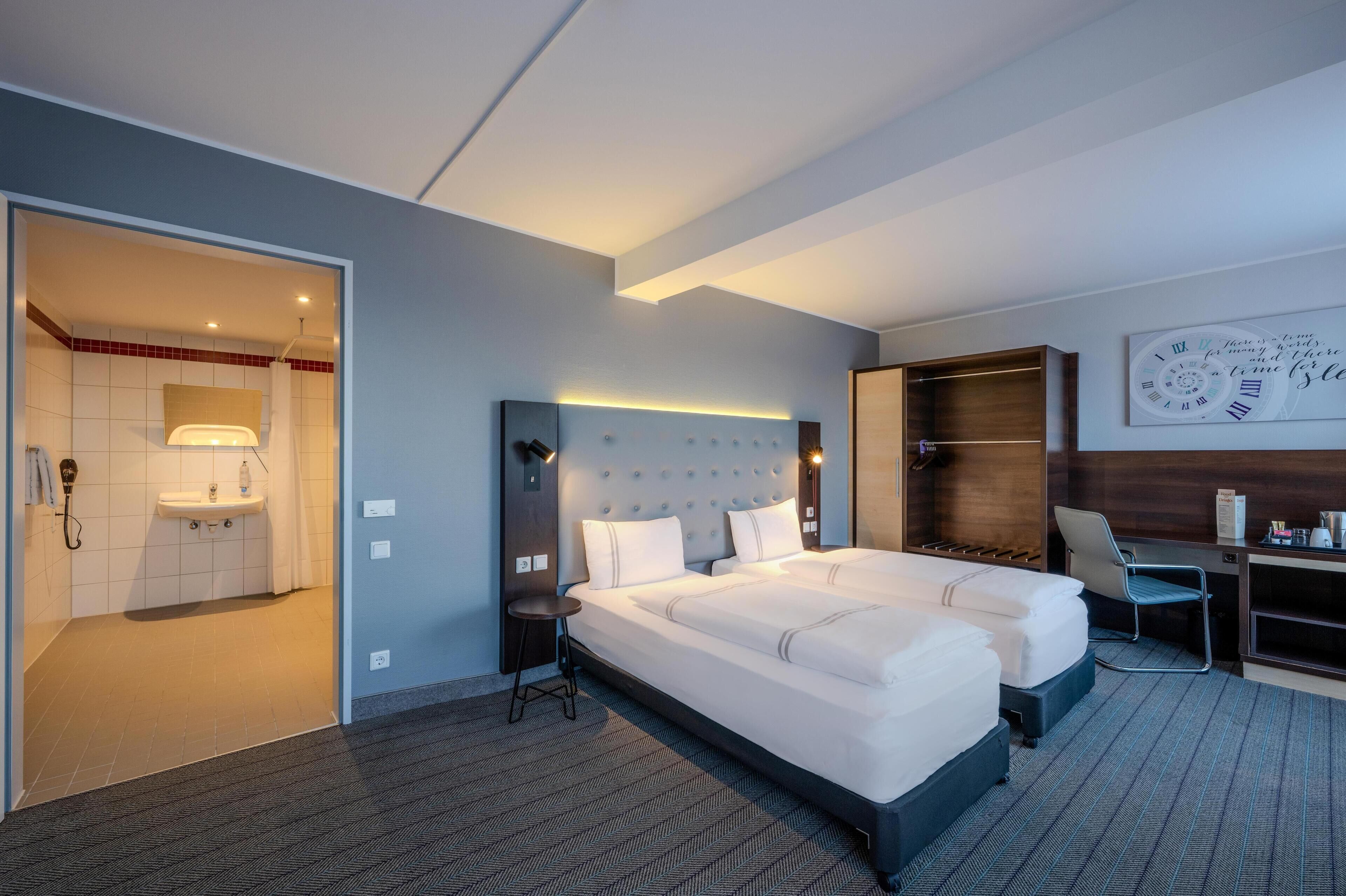 Ein Hotelzimmer mit einem großen Bett, einem Schreibtisch, einem Stuhl, einem Kleiderschrank und einem Badezimmer mit Waschbecken und Spiegel.