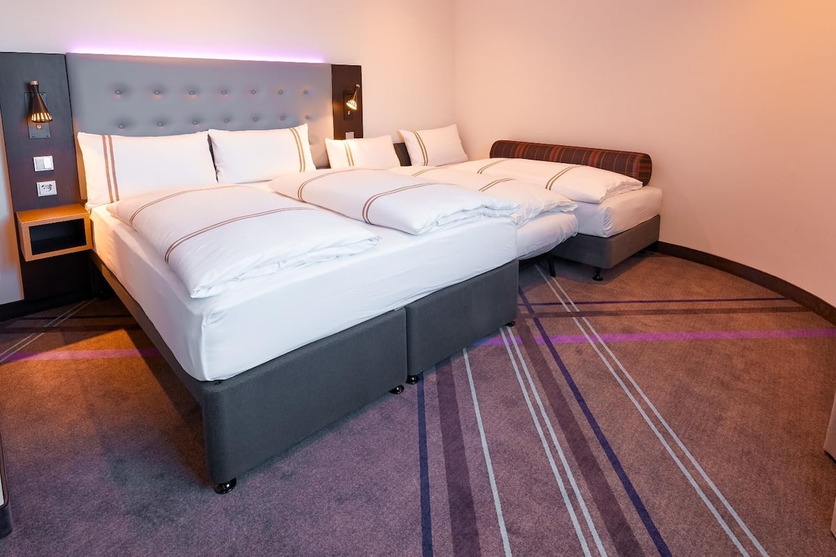Et hotelværelse med en stor seng, en mindre sofa, et natbord og en vægmonteret lampe.
