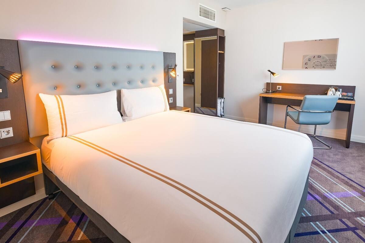 Et hotelværelse med en stor seng, et skrivebord, en stol og et spejl.