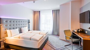 Hotellihuone, jossa on suuri sänky, työpöytä, tuoli, televisio ja ikkuna, jossa on verhot.