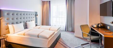 A hotel room with a large bed, a desk, a chair, a television, and a window with curtains.