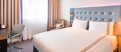A hotel room with a large bed, a chair, a desk, and a window with curtains.
