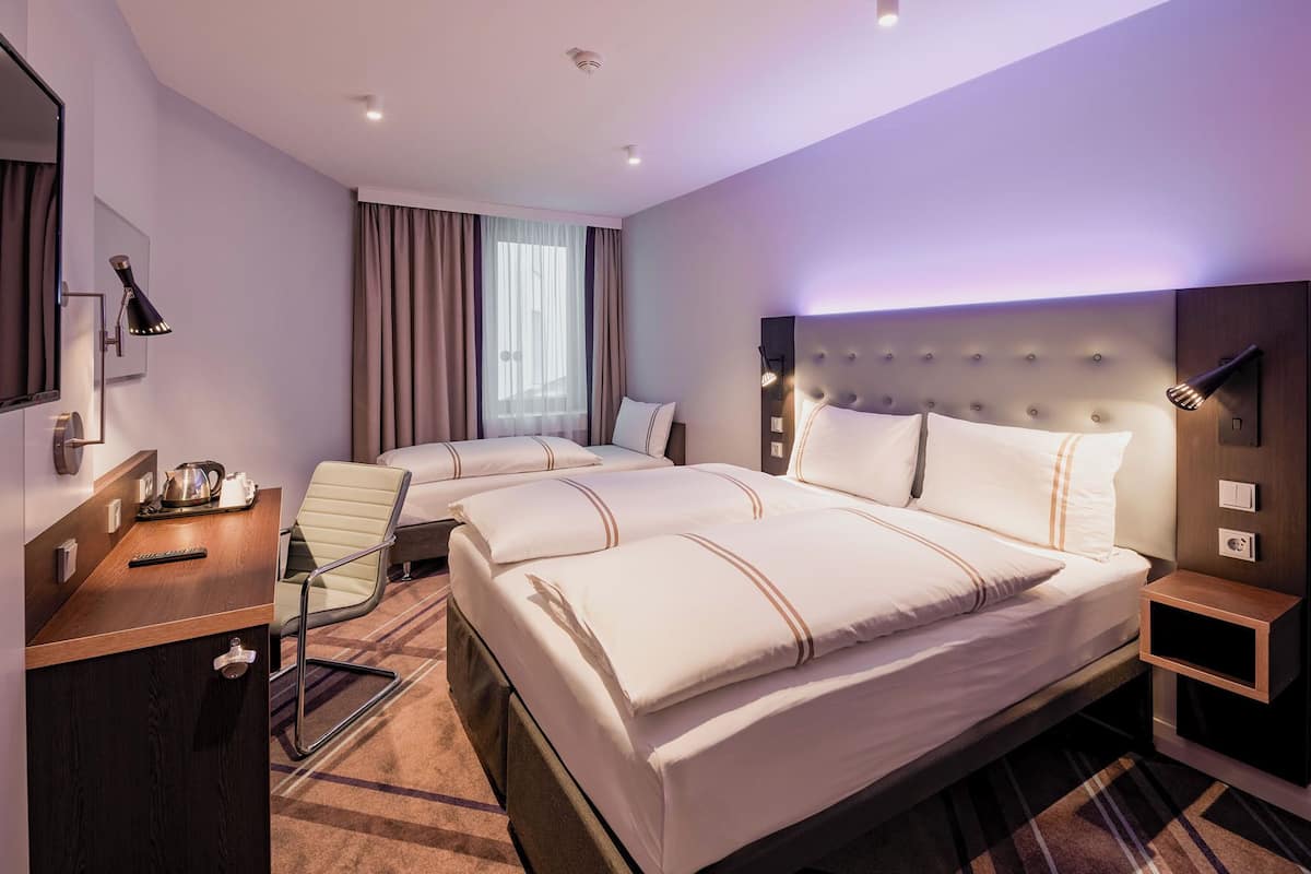 A hotel room with a large bed, a desk with a chair, a small table, and a mirror.