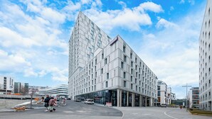 Un hôtel moderne, avec un bâtiment imposant situé à l’angle d’une rue, de grandes fenêtres en verre et un ciel dégagé.