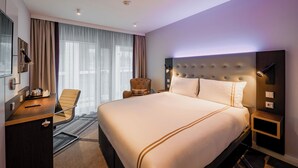 Une chambre d’hôtel avec un grand lit, un bureau avec une chaise, une télévision et un luminaire fixé au mur.