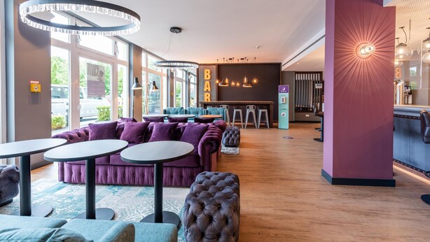 A modern bar area with round tables, a purple sofa, and pendant lighting. - Premier Inn München Airport Ost (Oberding)