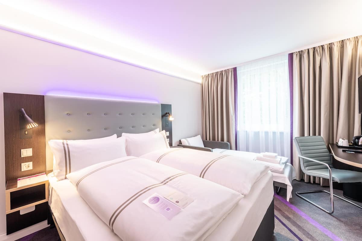 A hotel room with two beds, a desk, a chair, a headboard, and a window with curtains.