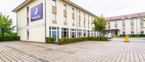 Un hotel con un llamativo letrero de Premier Inn, un patio empedrado y un edificio con múltiples ventanas.