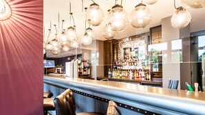 A bar area with leather chairs, a bar counter, and hanging light fixtures. - Premier Inn München Airport Ost (Oberding)