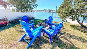Eine Terrasse mit blauen Adirondack-Stühlen und einem Feuerkorb, mit Blick auf ein Gewässer.