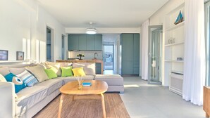 A modern living room with a sofa, a coffee table, and a kitchen in the background. - Villa Helia With Swimming Pool (Paros)